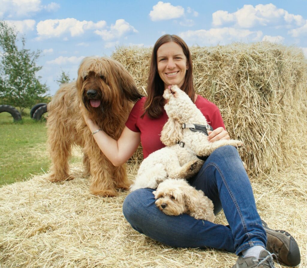 Manja Hund Heu. Zwei Hunde spielen mit Frau im Heu, Bauernhofatmosphäre